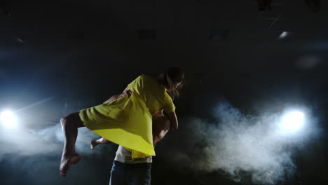 Die-Kamera-Zoomt-Und-Schießt-In-Zeitlupe-Von-Der-Vollaufnahme-Zur-Mittelaufnahme-Ein-Junges-Mädchen-In-Einem-Gelben-Kleid-Und-Einen-Mann-In-Einem-Weißen-Hemd,-Die-Im-Scheinwerferlicht-Und-Rauch-Auf-Der-Bühne-Tanzen